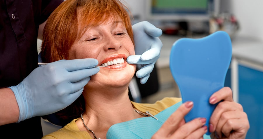 Dentures 1 lady holding a mirror while fitting her new denture with the assistance of a dentist