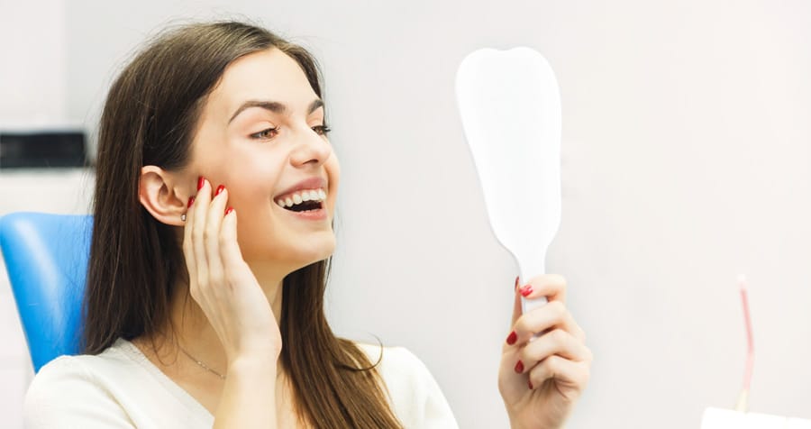 Restorative Dentistry 1 happy woman smiling and admiring her smile in the mirror.