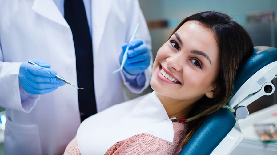 Dental Exams 1 smiling woman showing her teeth during a dental exam with a dentist beside her in a clinic