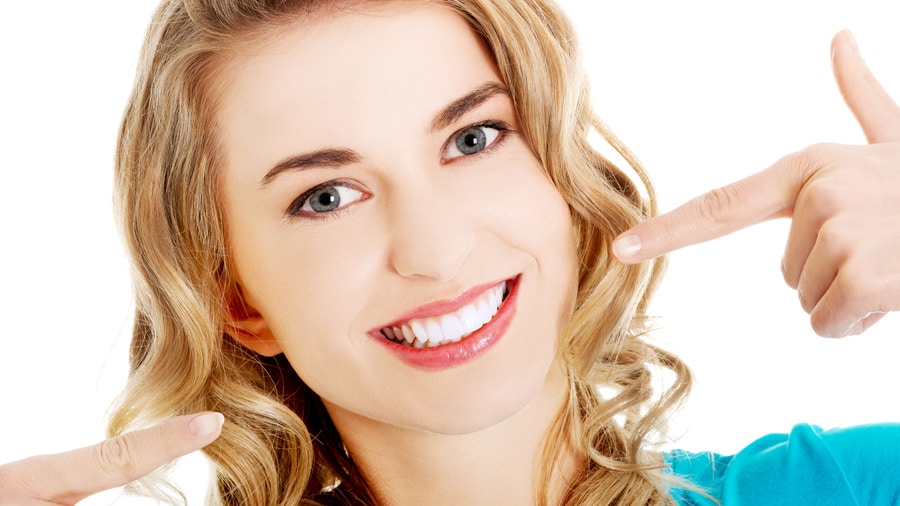 Cosmetic Dentistry 1 woman smiling and pointing to her bright white teeth