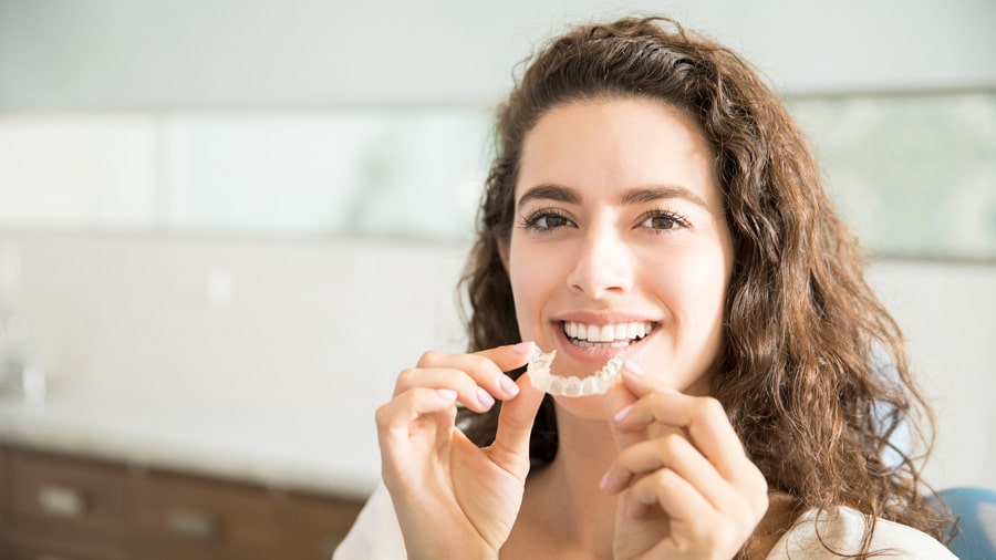 Sure Smile Clear Aligners 1 smiling woman holding SureSmile aligners, showcasing a confident and bright smile